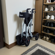 A foldable, four-wheeled Bion Rollator Q100 walker with a black storage bag, gray frame, and black wheels, folded.